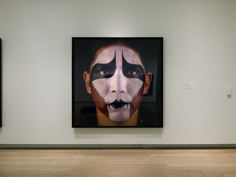 A photograph of Indigenous person with face paint in an art gallery.