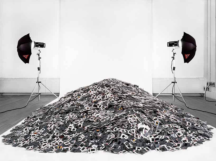 A black-and-white photo of a pile of polaroid pictures in front of two traditional projectors. 
