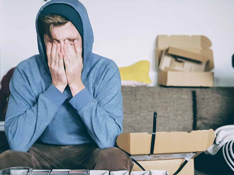 An exhausted man sits on a couch with his hands covering his face. 