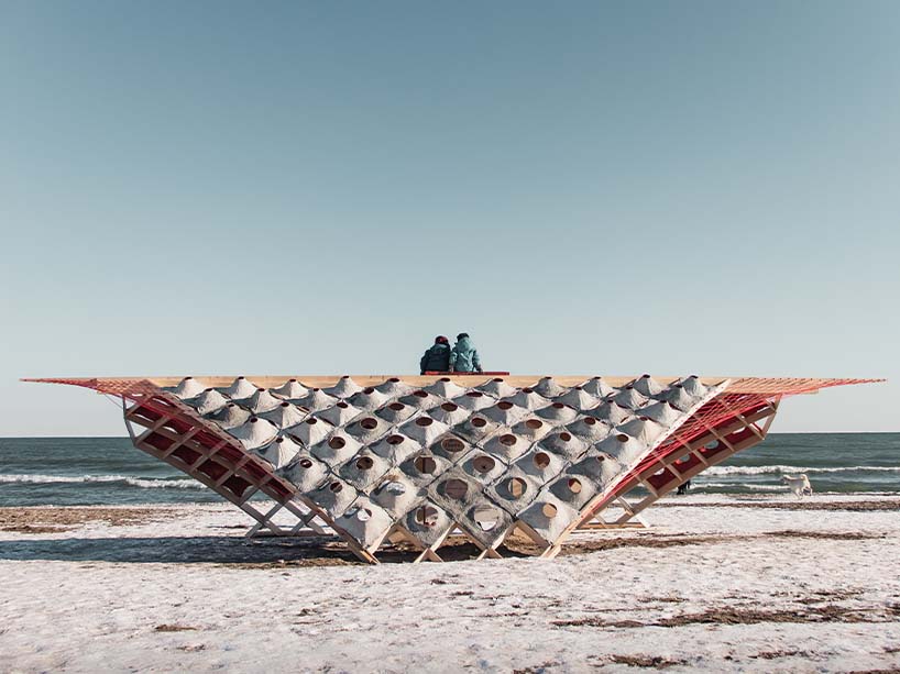 Two people sit on an art installation at the beach in winter