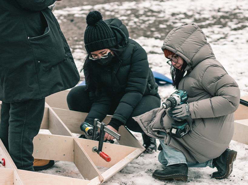 Three students build a wooden structure outside