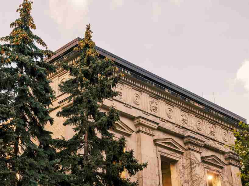 The top of university building facade behind tall trees.