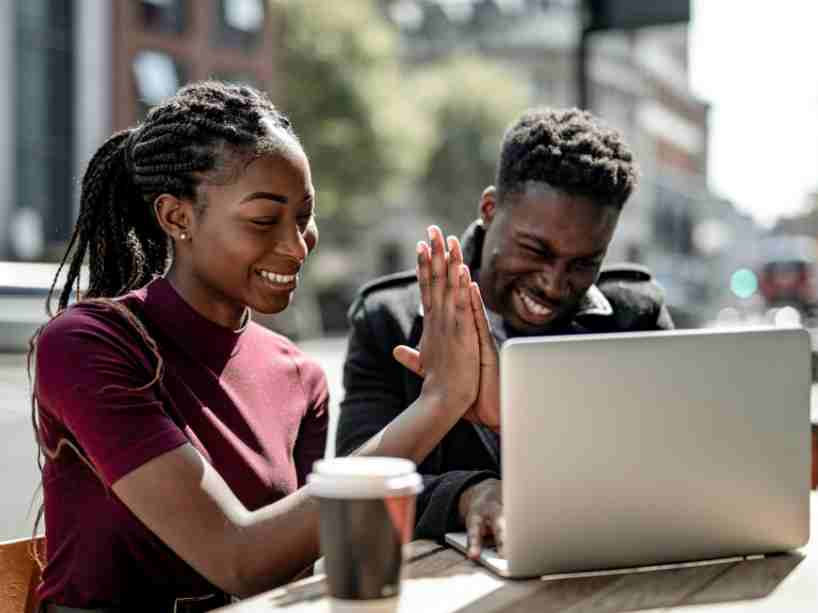 Two Black students high-fiving in front of a laptop in a cafe