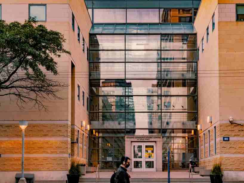 A person wearing a mask walks in front of a campus building.