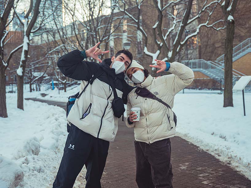 Two students walking together on the path in the Quad wear masks.