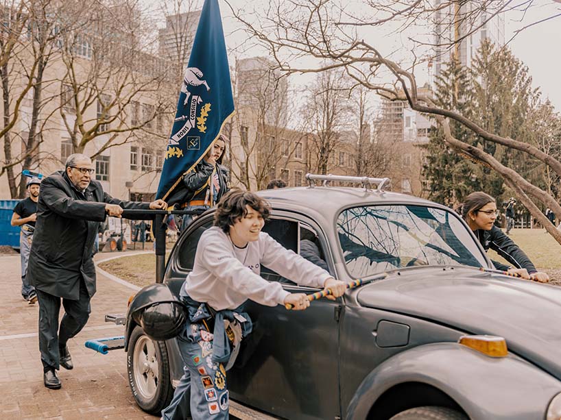 A group of four people push a vintage Bug along a cobbled walkway.