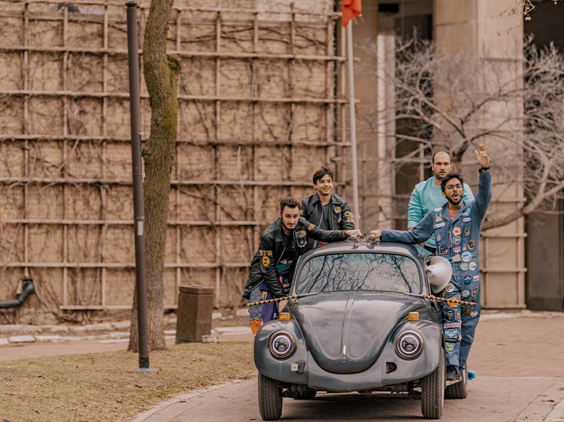 Four people push a vintage Volkswagen Beetle around the Ryerson quad.