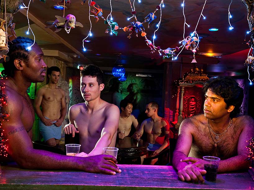 Shirtless men sitting at a bar.