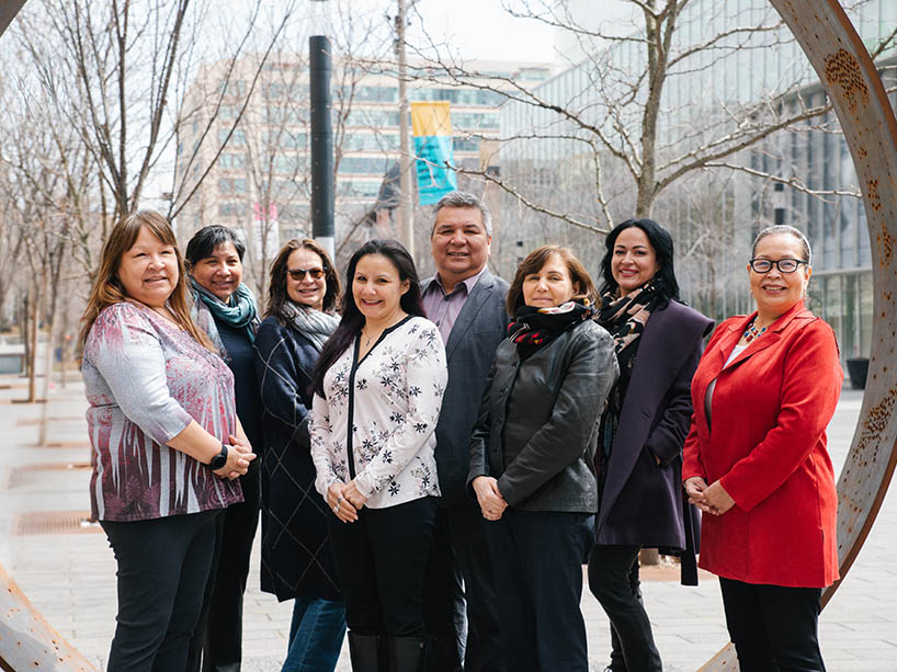 Sheila Saikkonen, Amy Desjarlais, Sloan Miller, Cher Trudeau, Brian Norton, Diane Simone, Sarena Johnson and Monica McKay stand in front of The Ring sculpture on campus.