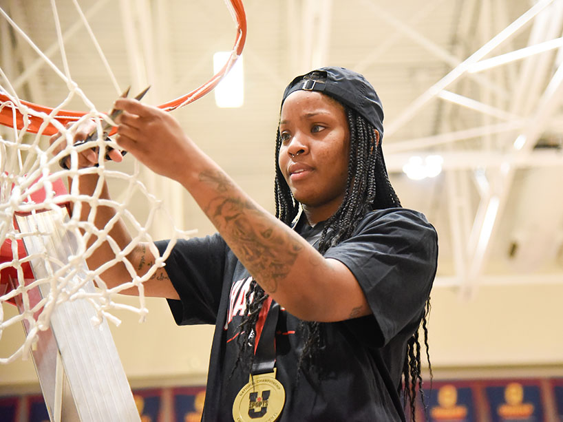 Kyia Giles cuts a piece of net from a basketball hoop.