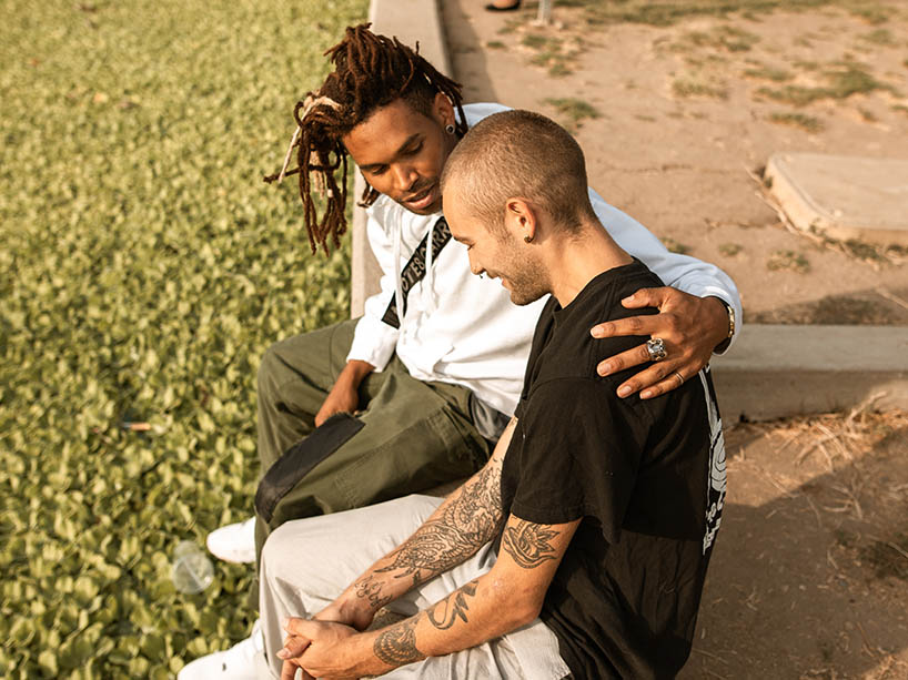 Two men sitting on a curb embracing.