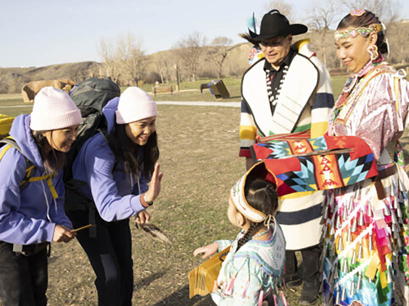 Two women in matching outfits are greeted by three people in Indigenous regalia