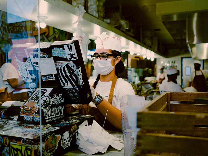 A young woman is working in a restaurant with a mask on.