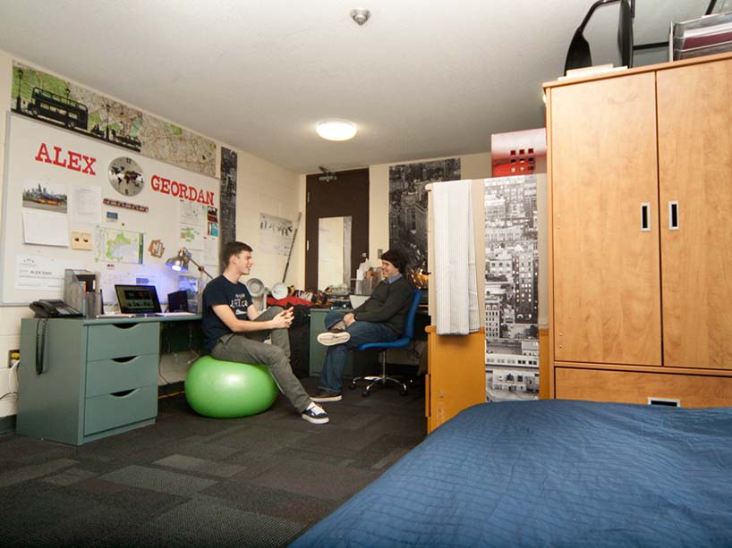 Two young men sit in a residence room engaged in conversation.