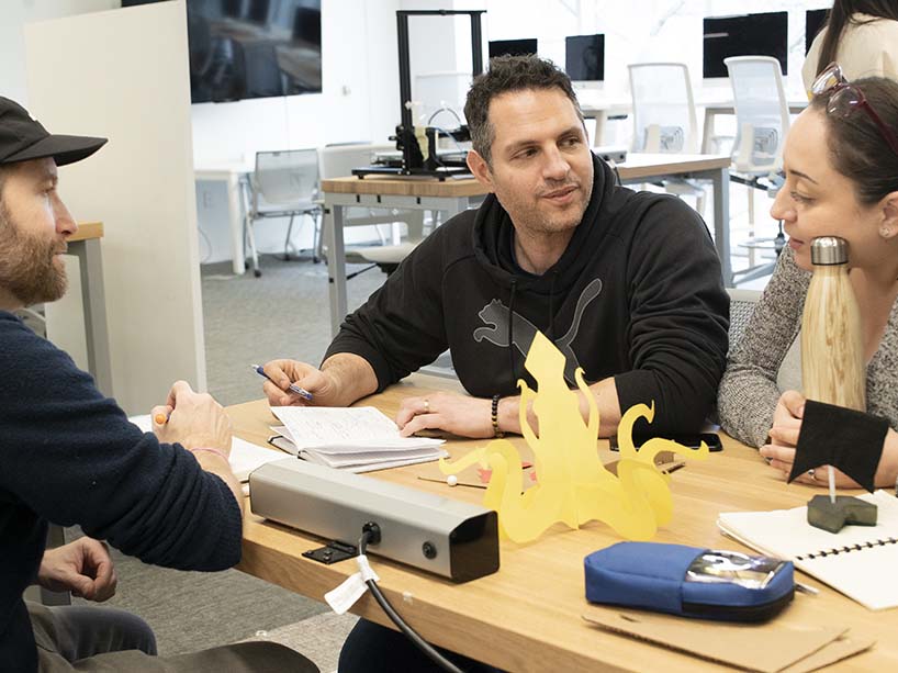 Three adult learners around a table with yellow squid-shaped paper concept for a toy
