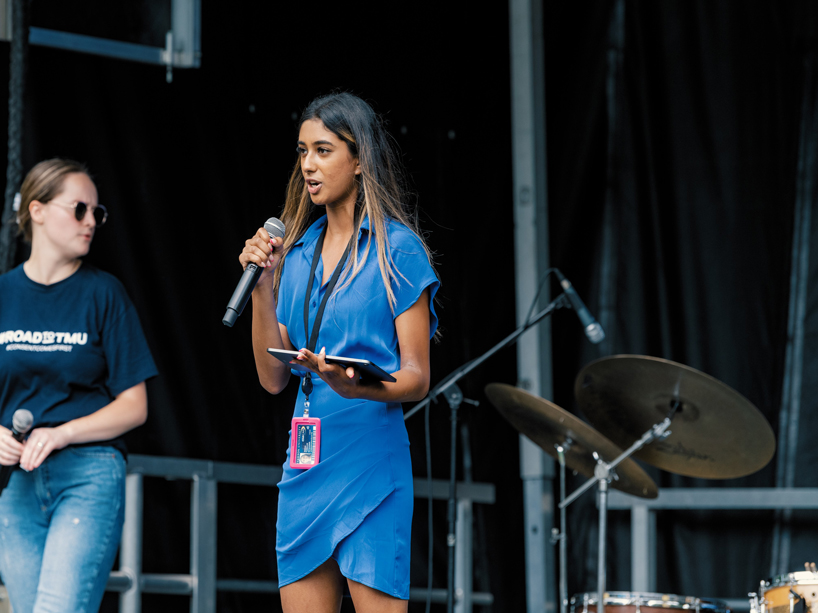 Sonia Tumkur speaks into a microphone on stage.