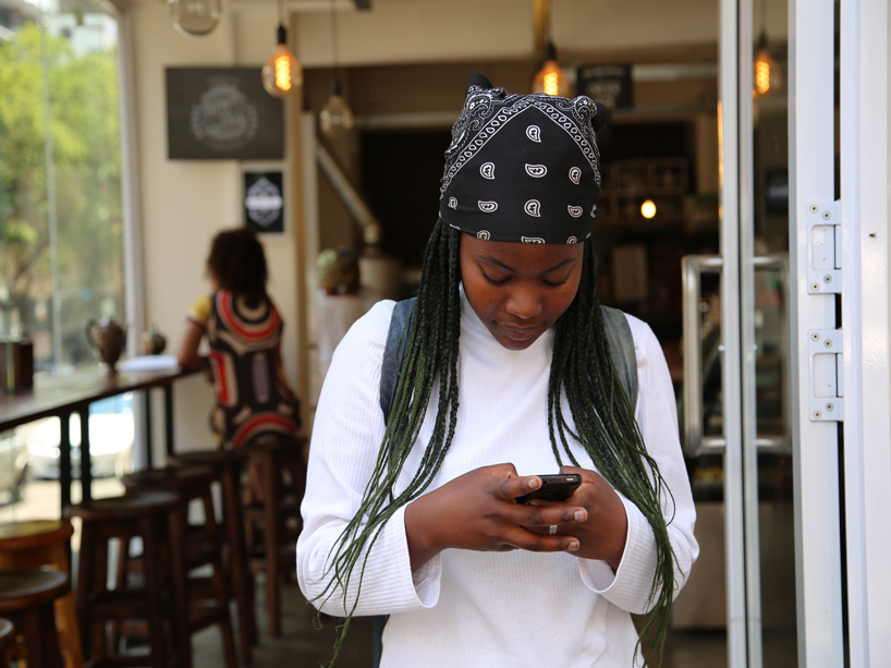 A young woman looks down at her phone while standing in a coffee shop. 