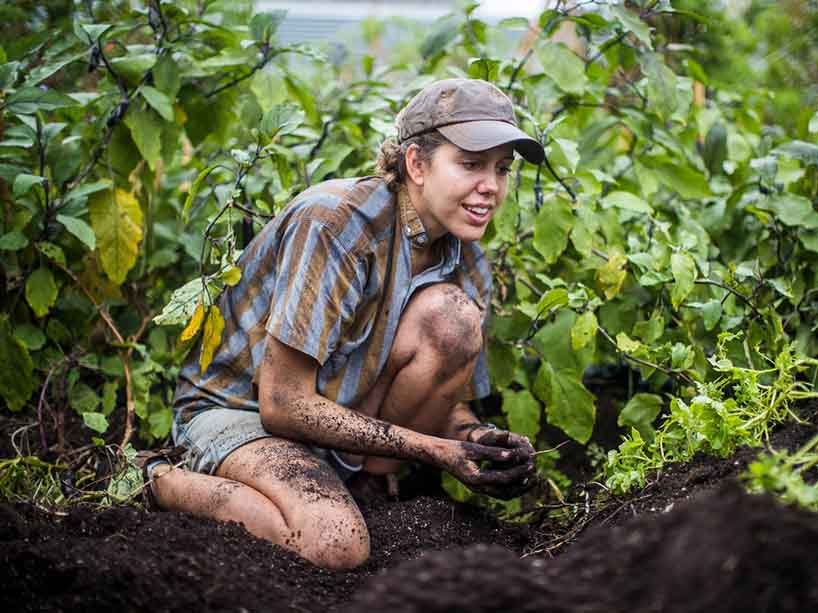 Woman kneels in a garden with dirt in her hands.