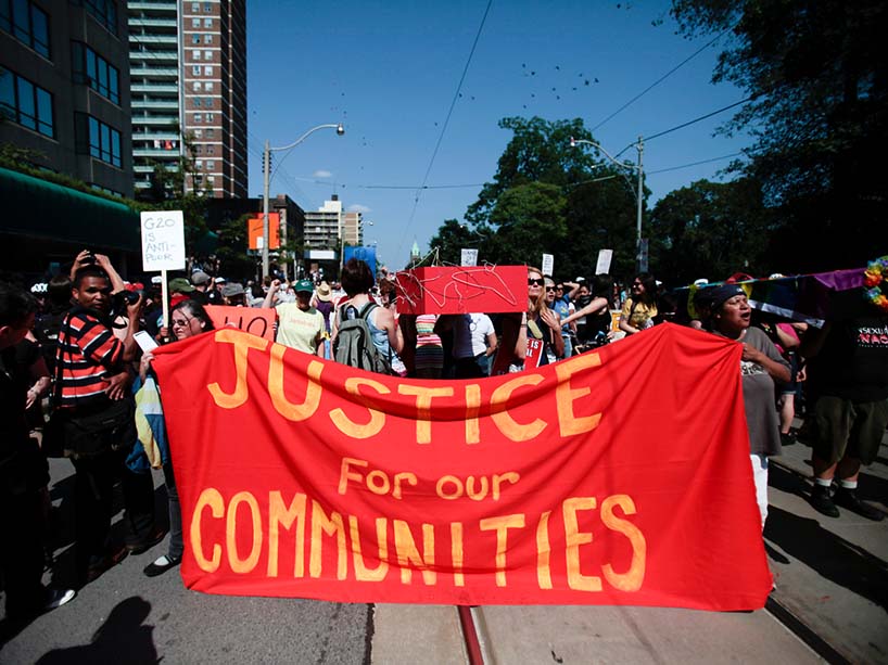 Protestors hold up a red banner reading ‘Justice for our Communities’.