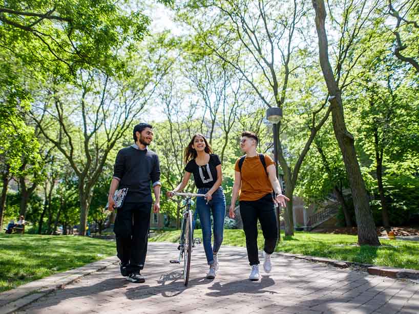 Three students walking outside with a bicycle.