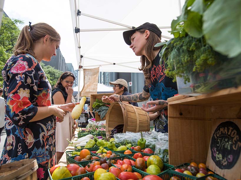 Young woman holds zucchini at a farmer’s market table on campus