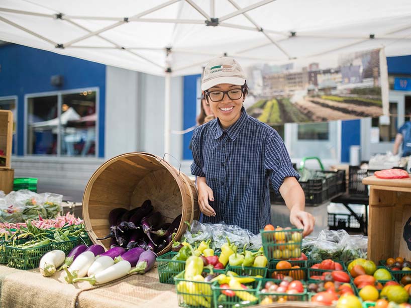 Young woman at a farmer’s market table displaying colourful vegetables