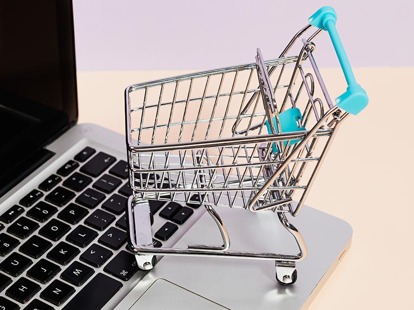 Open laptop with miniature shopping cart sitting on top.