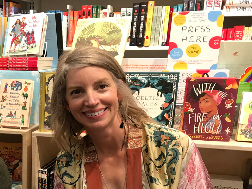 Sarah Henstra in a patterned blouse with a bookshelf behind her