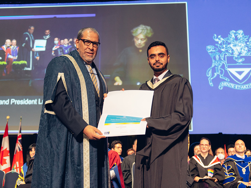 MBA graduate Harsh Brahmbhatt holds his gold medal certificate while standing next to TMU President Mohamed Lachemi at the Fall 2022 convocation ceremony.