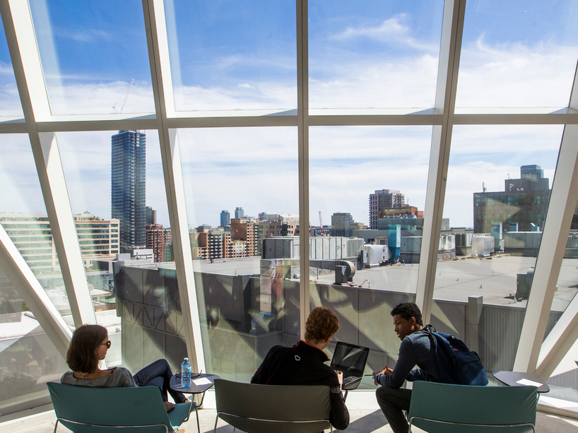 Three students sitting inside the Student Learning Centre facing tall windows looking out to the city