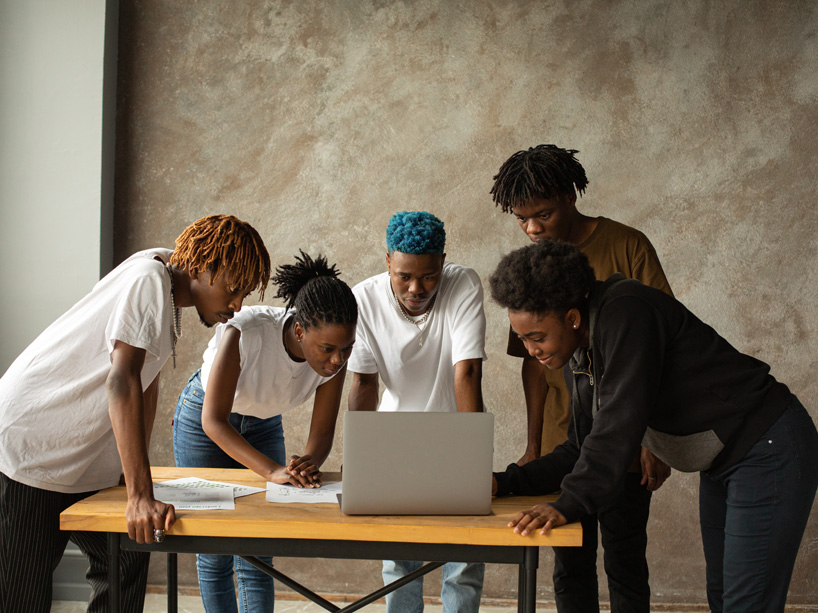 Young Black students stand around a computer.