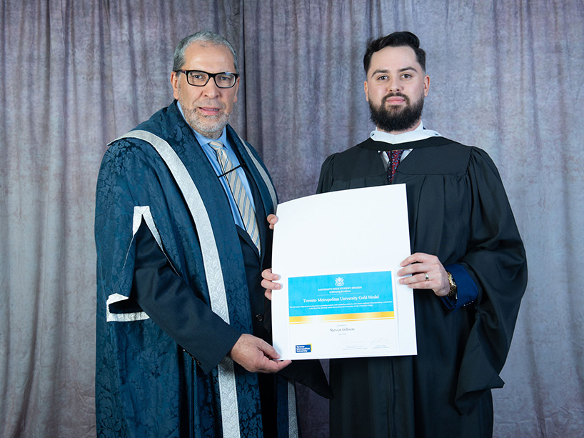 Steven Gibson holds his gold medal certificate while standing next to TMU President Mohamed Lachemi at Fall 2022 convocation.