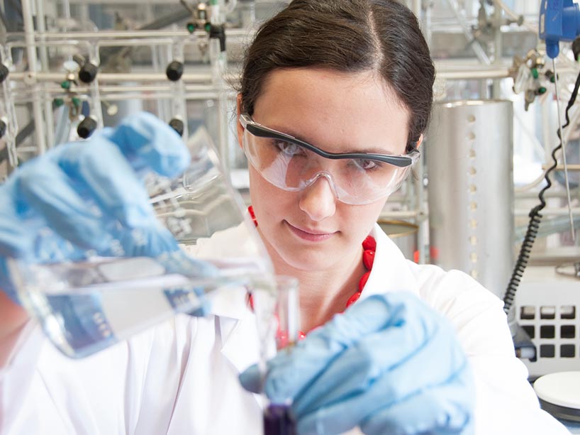 Woman with lab goggles pouring liquid into the test tube.