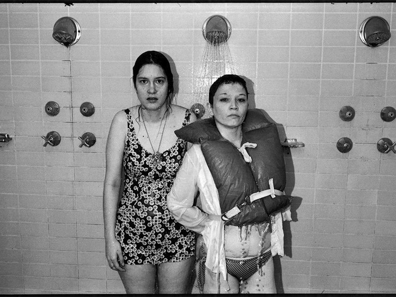 Two women in bathing suits stand in a shower.