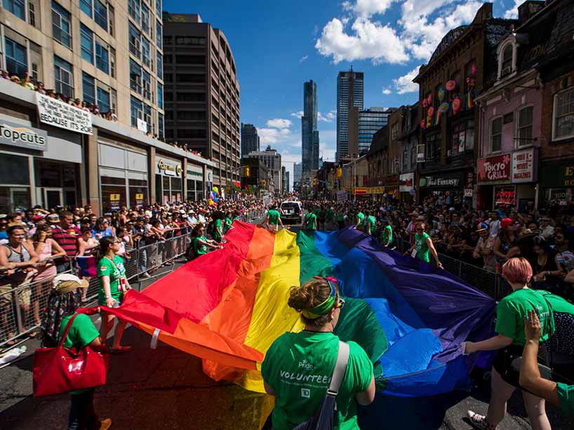 Large Pride parade flag being held by numerous volunteers
