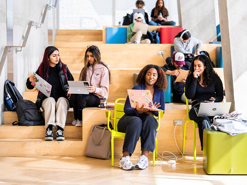 A group of students sitting on stairs studying and talking with laptops on their laps.