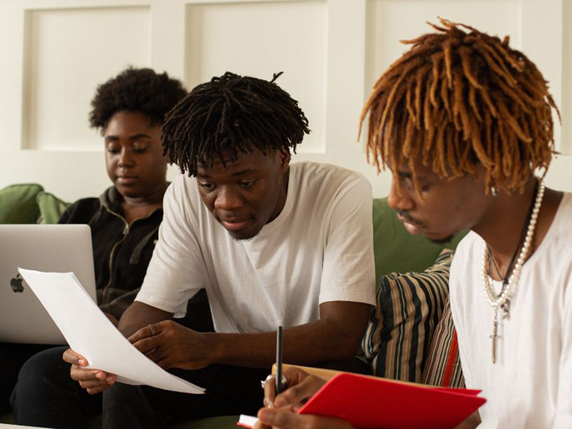 Three people sit at a table looking at papers.