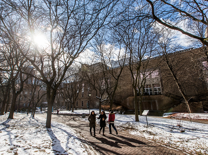 Three students walking through a snowy university campus.