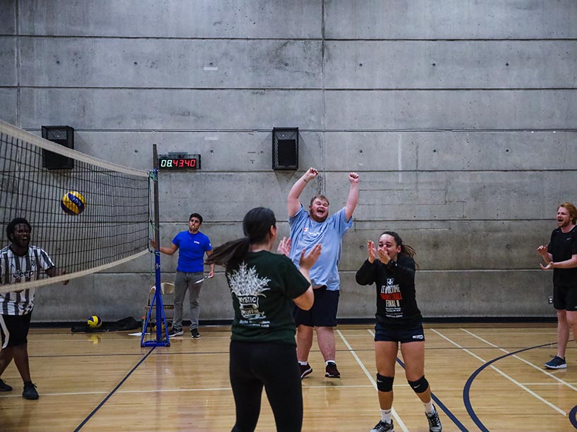 A group of students celebrate a volleyball play from the court.