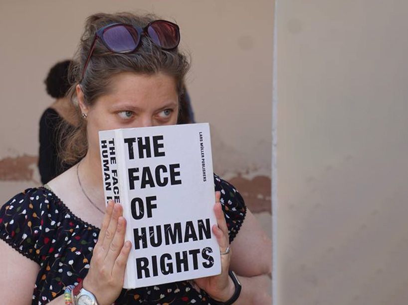 Alissa Novitchkova holds a book over her face which is titled, "The face of human rights" during the Venice Summer School of Human Rights in 2016.