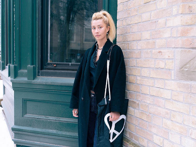  Benet Avery wearing a black coat against a brick wall. 
