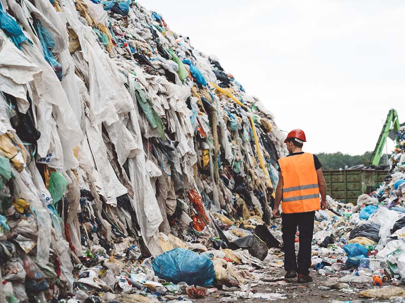 A worker walks between massive piles of garbage and clothing waste. 