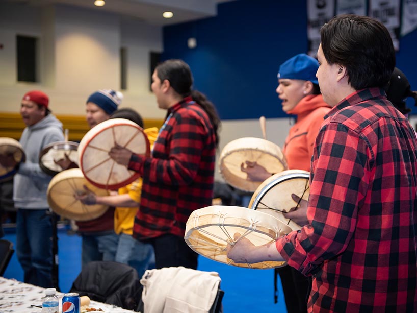 A group of people standing around each other playing hand drums and singing.