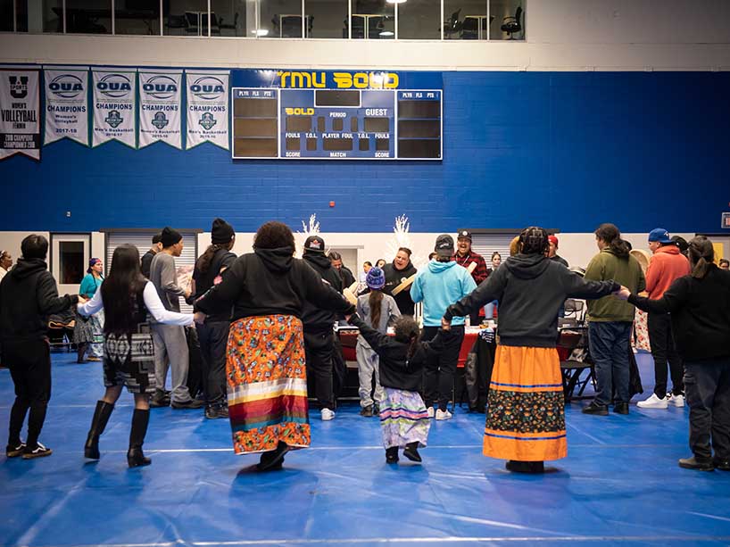 A group of people holding hands in a big circle around a table.