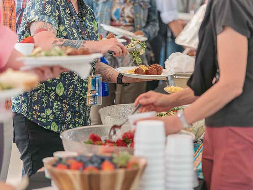 People make their way through a buffet, filling their plates with food.