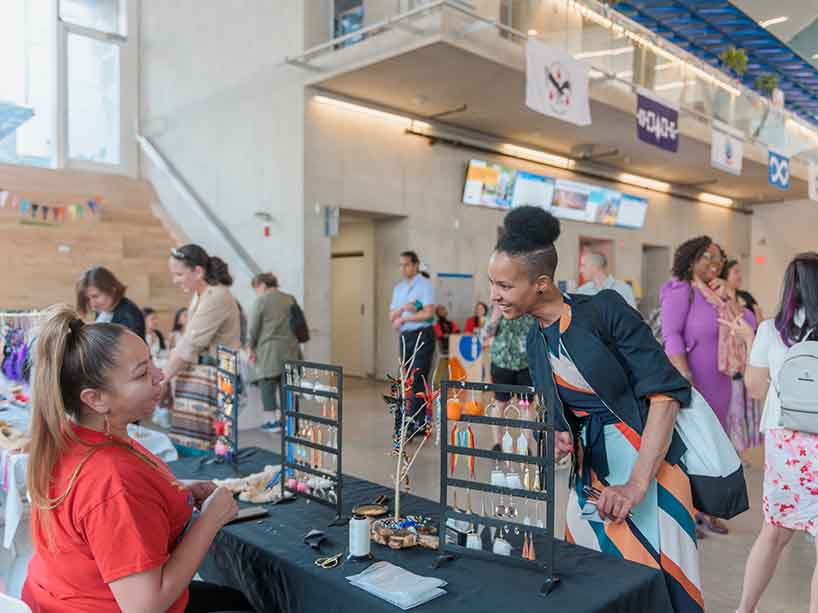 A community member speaks with one of the Indigenous vendors at their table selling handmade jewelry. 