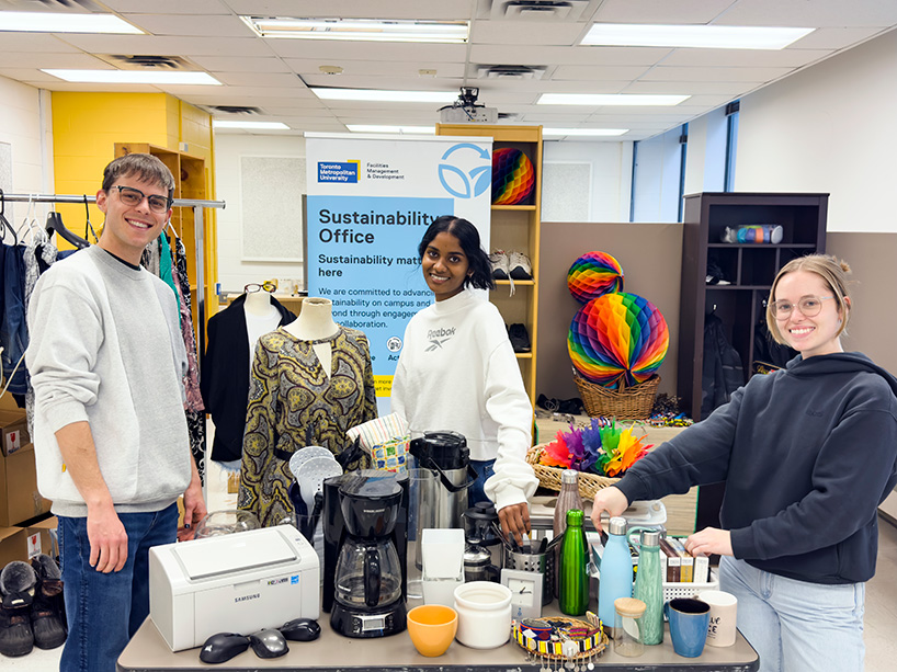 Three students gathered around a table with secondhand items.