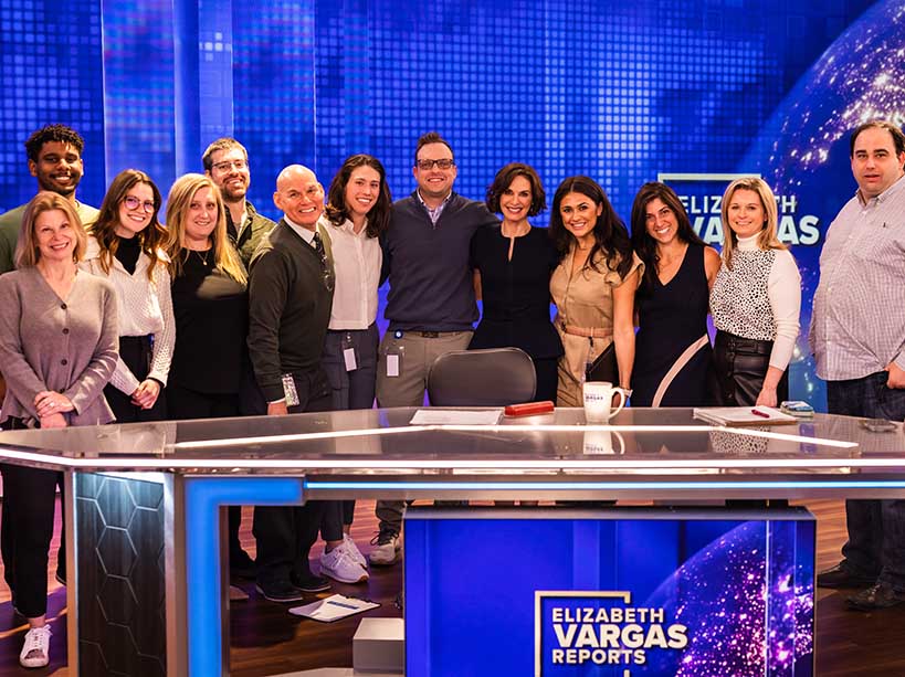 A group of people behind a news desk on set.