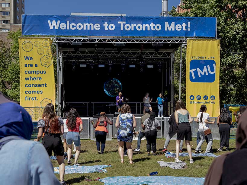 People dancing in front of a stage with TMU banners. 