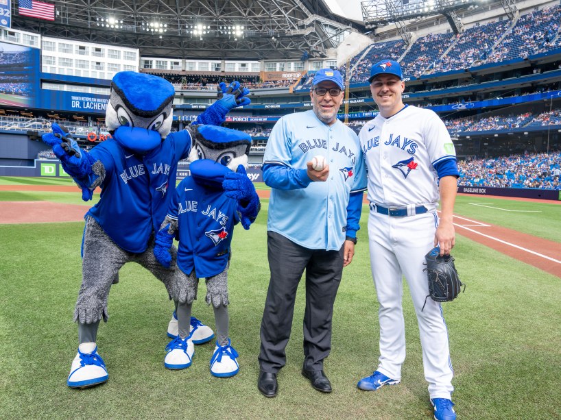 President Mohamed Lachemi holds a baseball in Rogers Centre, standing next to pitcher Erik Swanson and two Blue Jays mascots.